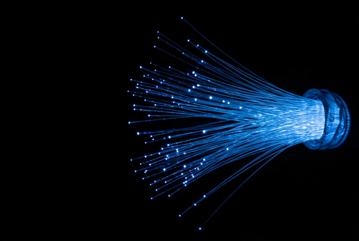 A cluster of illuminated optical fiber strands fanning out to the right against a solid black background.